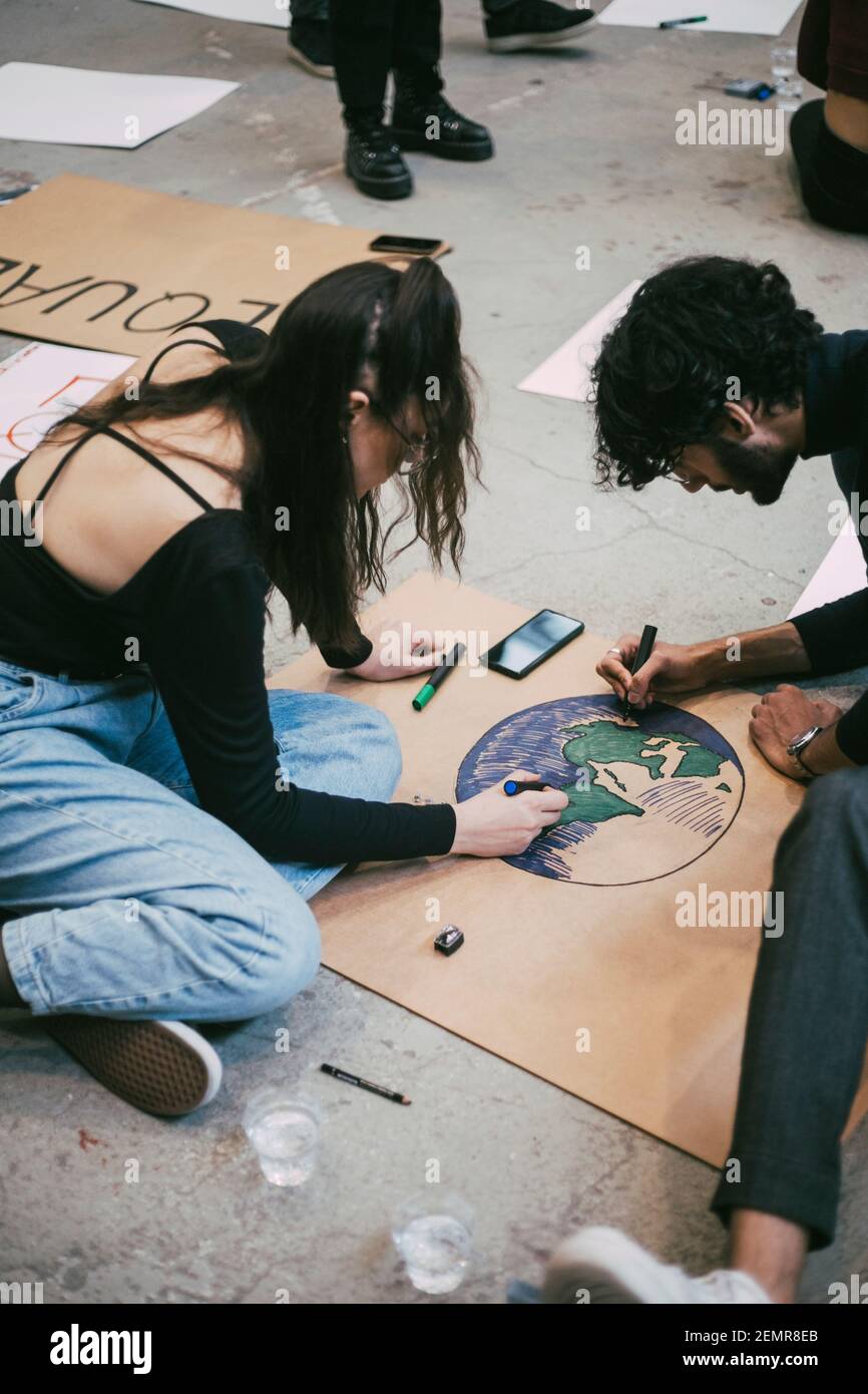 Male and female activists preparing signboard for environmental issue in building Stock Photo
