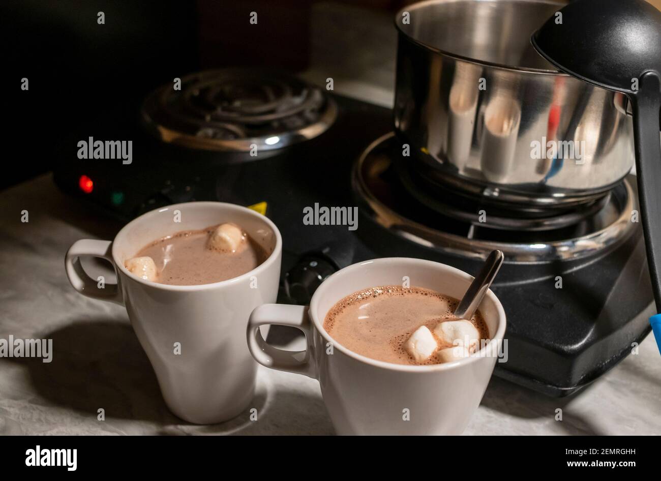 Two hot chocolate cups in front a portable electric burner stove at night Stock Photo