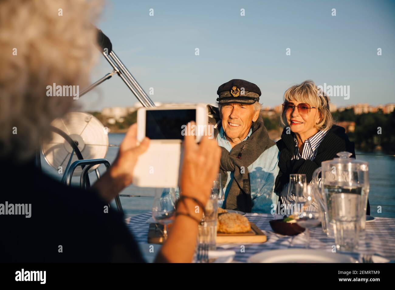 Cropped image of woman photographing senior couple sitting in boat on sunny day Stock Photo