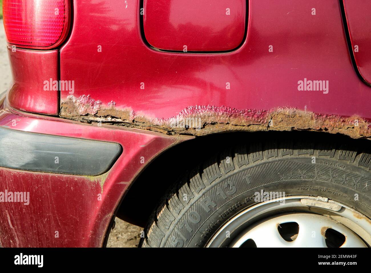 The detail of the holey and rusty fender of the older car. The ...