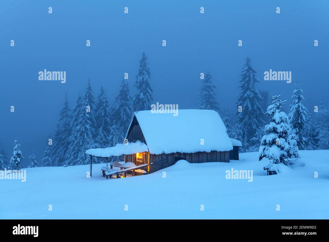 Fantastic winter landscape with glowing wooden cabin in snowy forest ...