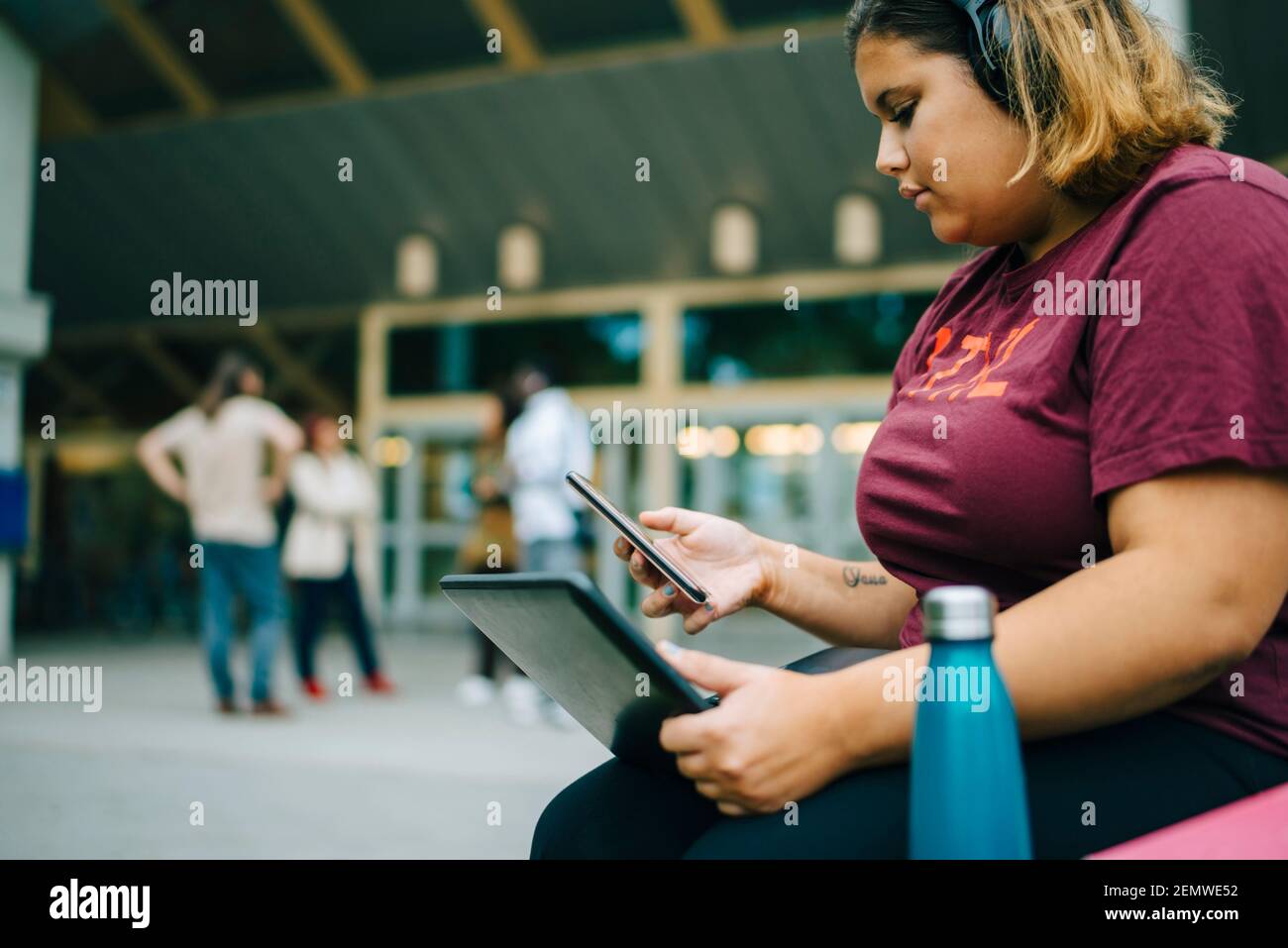 Female student with laptop using smart phone in university campus Stock Photo