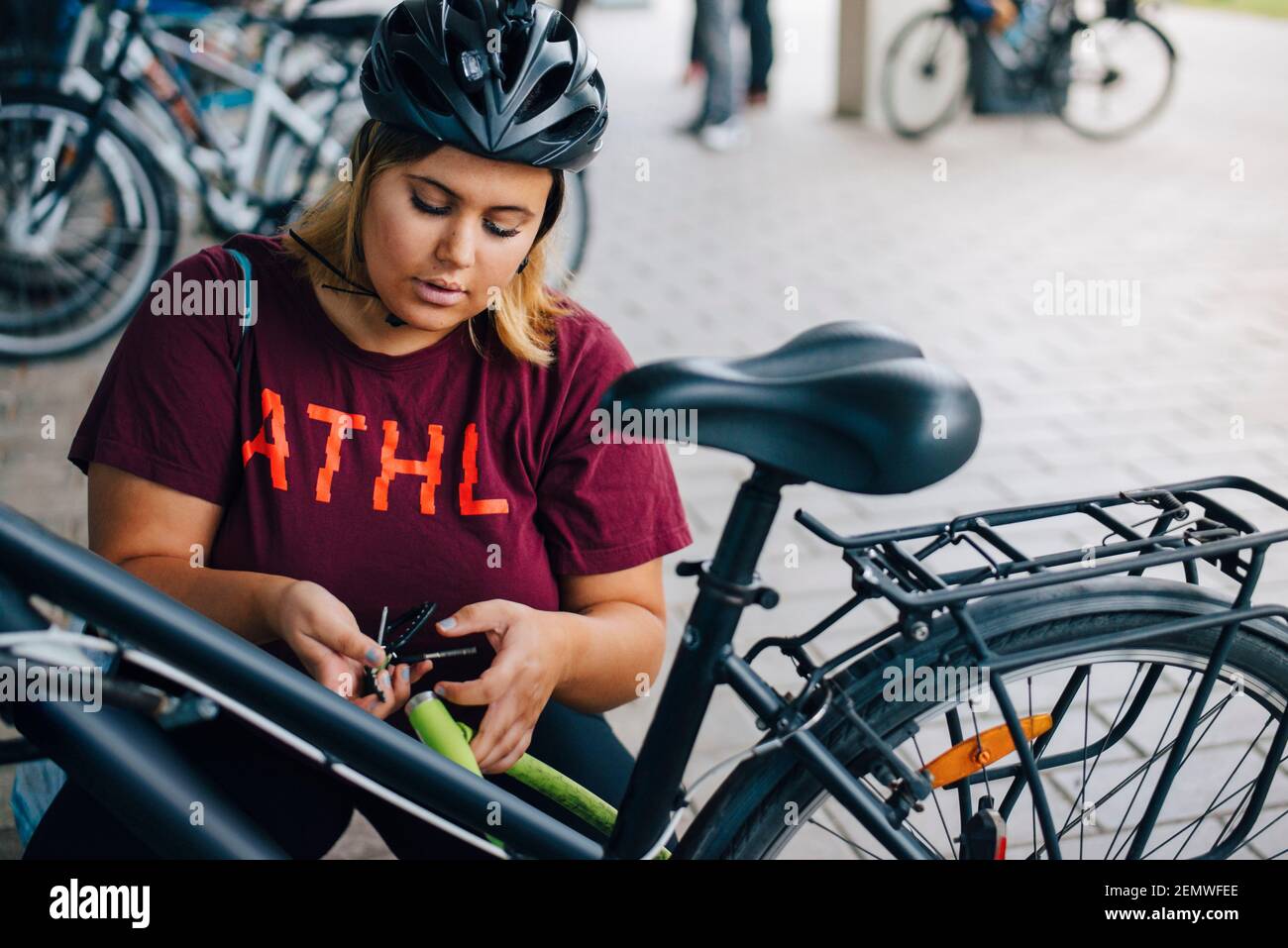 Young female student unlocking bicycle at parking station in university campus Stock Photo