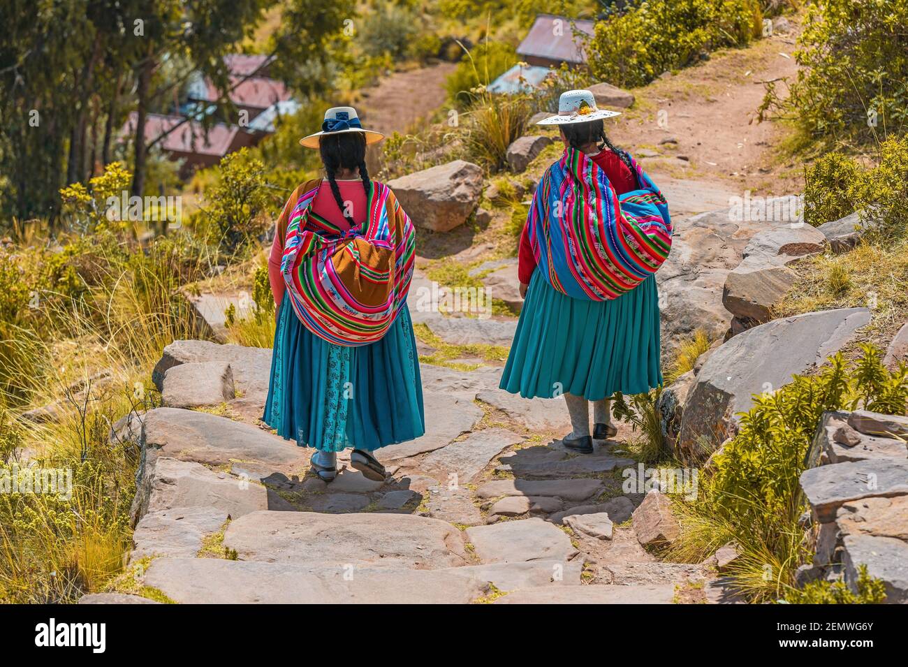 Two Peruvian indigenous Quechua women walking along a trail in traditional clothing and textile bag, Taquile Island, Peru. Stock Photo