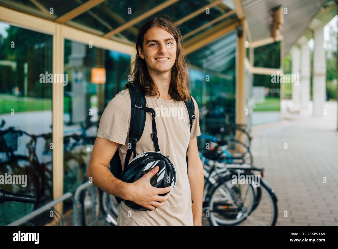 Portrait of smiling male student with cycling helmet at bicycle parking station in campus Stock Photo