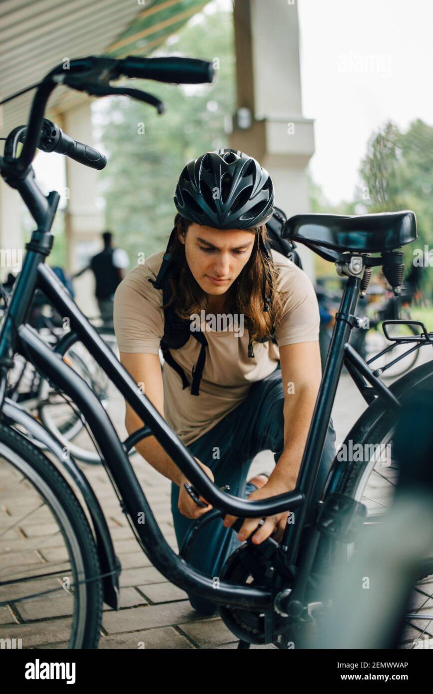 Male student unlocking bicycle at parking station in college campus Stock Photo