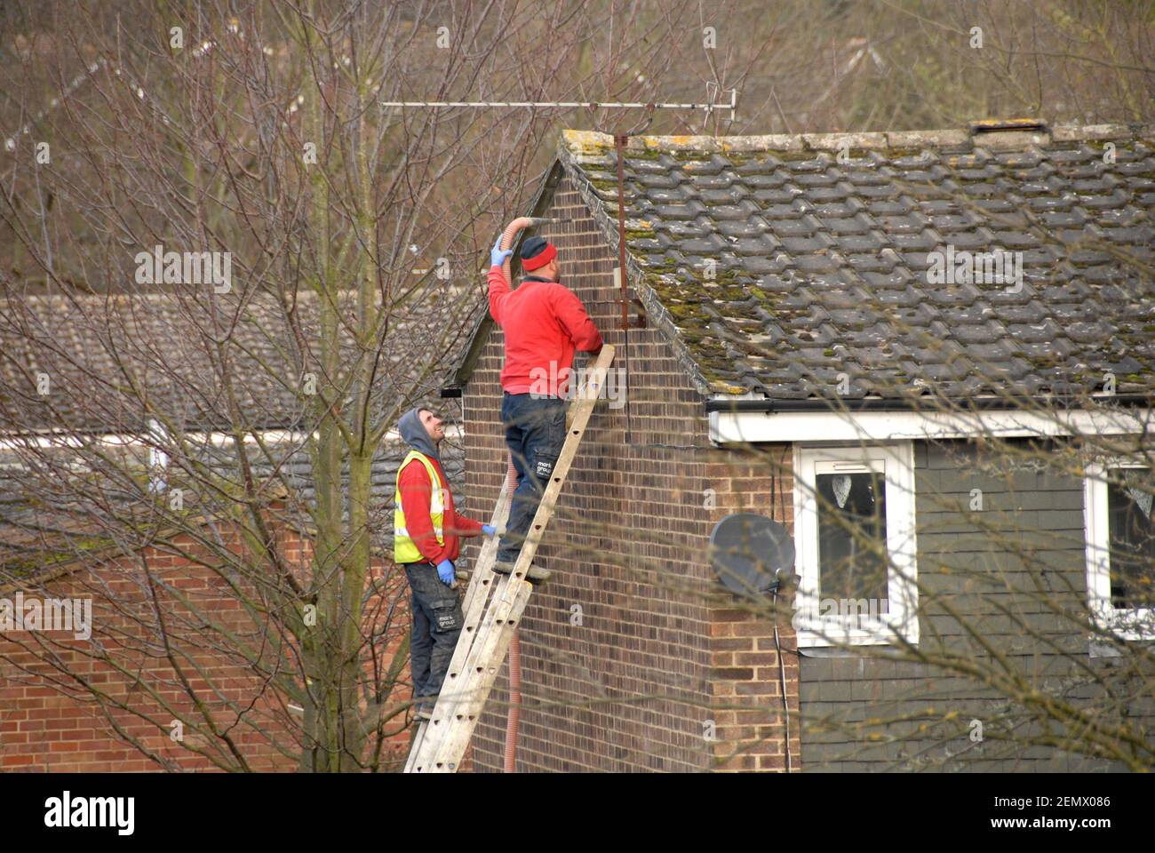 Two men working on ladders injecting insulation into cavity wall, Kent, England Stock Photo