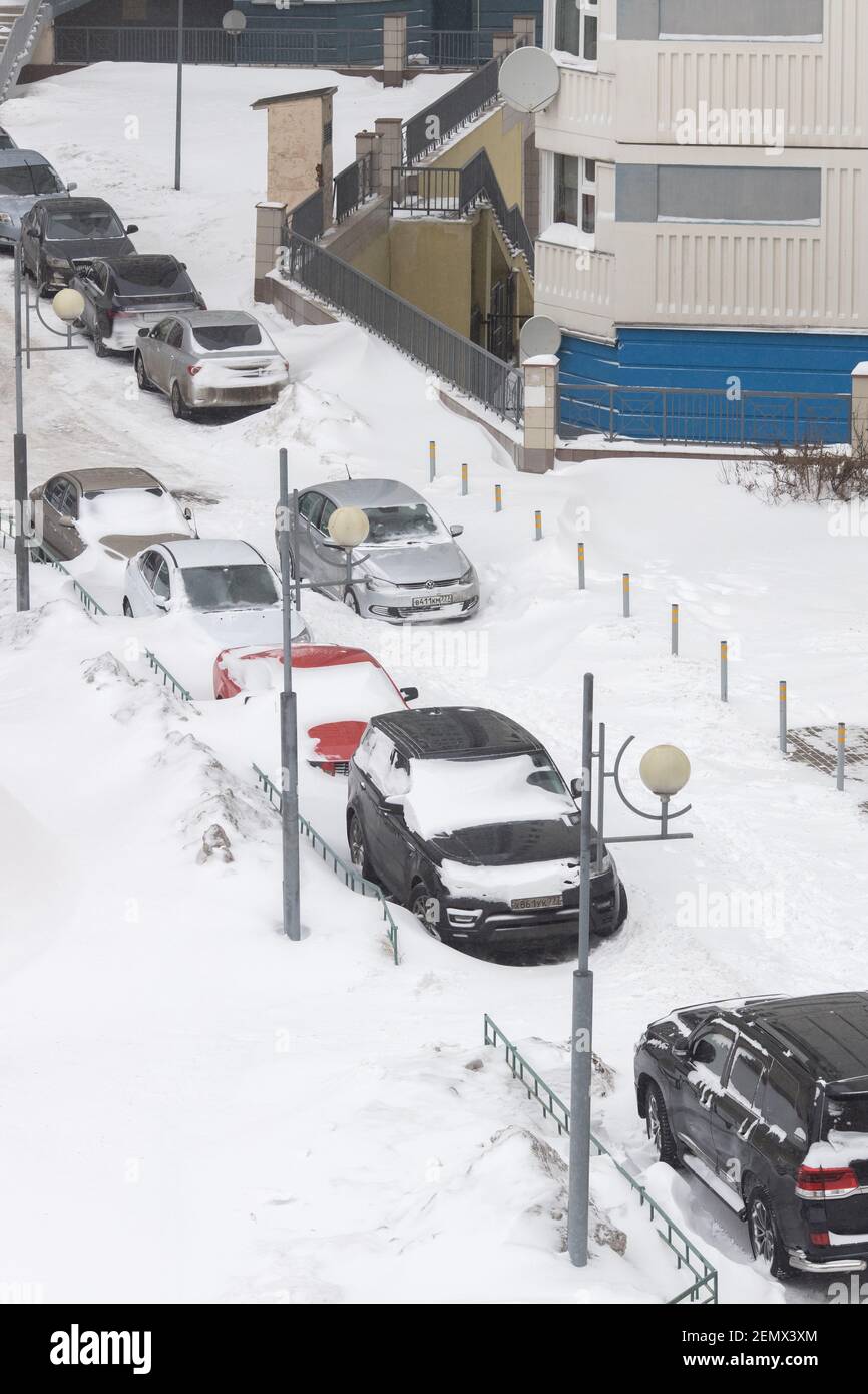 Moscow / Russia - February 13 2021: Cars in street parking near apartment building under thick layer of snow, one car got stuck right on road, after n Stock Photo