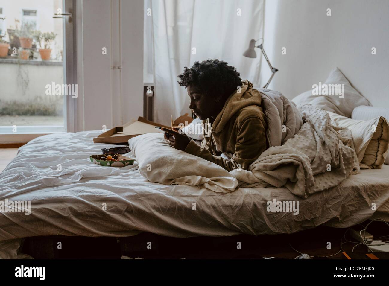 Young woman using smart phone while lying on bed at home Stock Photo