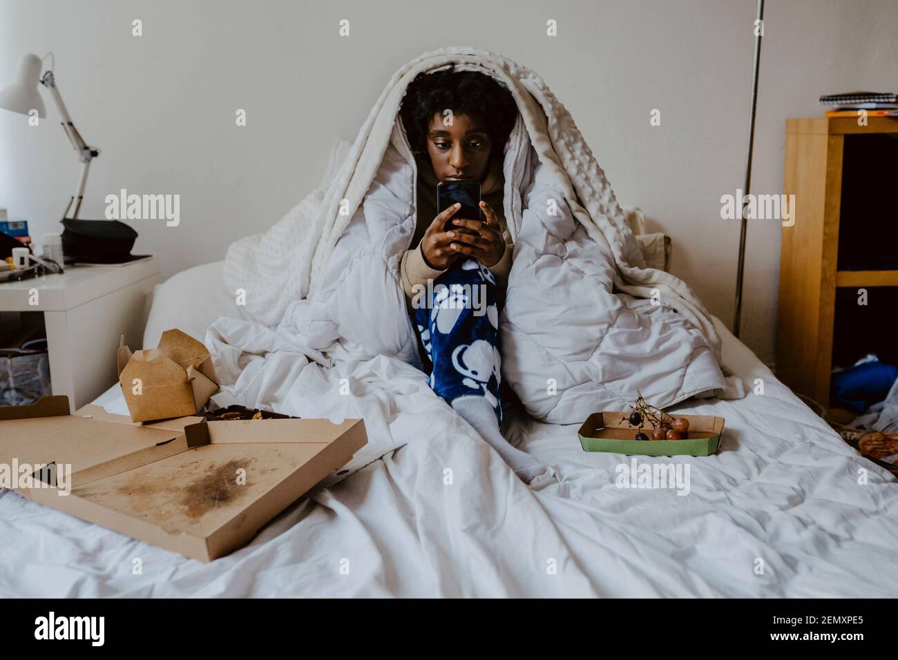 Young woman using smart phone while sitting in bedroom Stock Photo