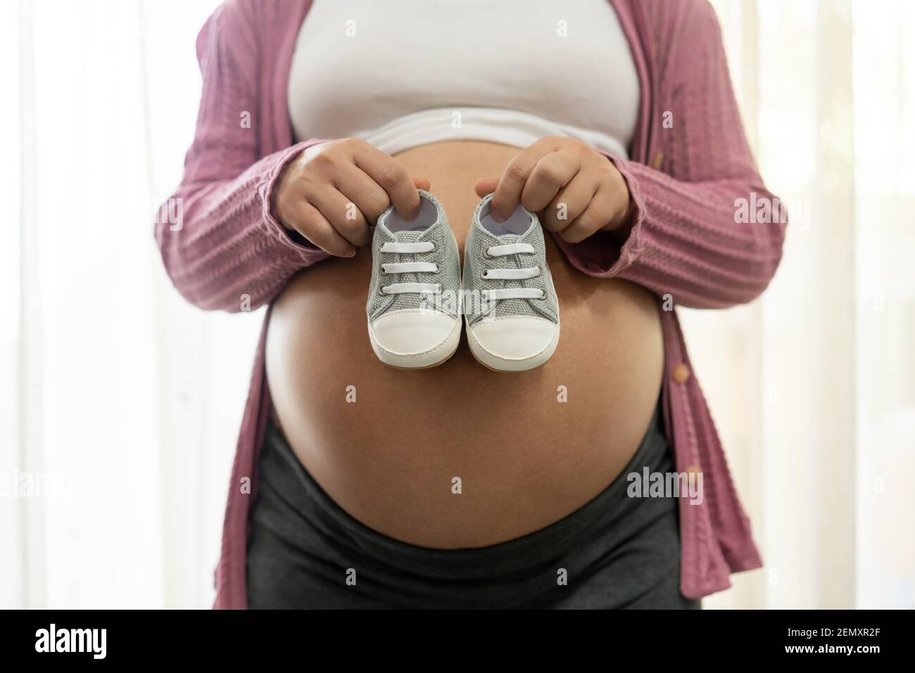 Pregnant woman feeling happy at home while taking care of her child. The young expecting mother holding baby in pregnant belly. Maternity prenatal Stock Photo