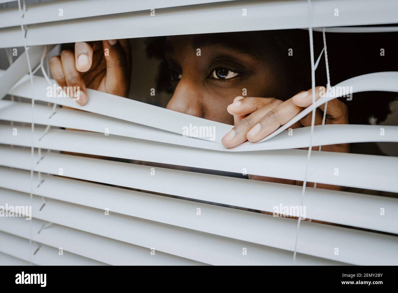 Depressed woman looking through window blinds Stock Photo