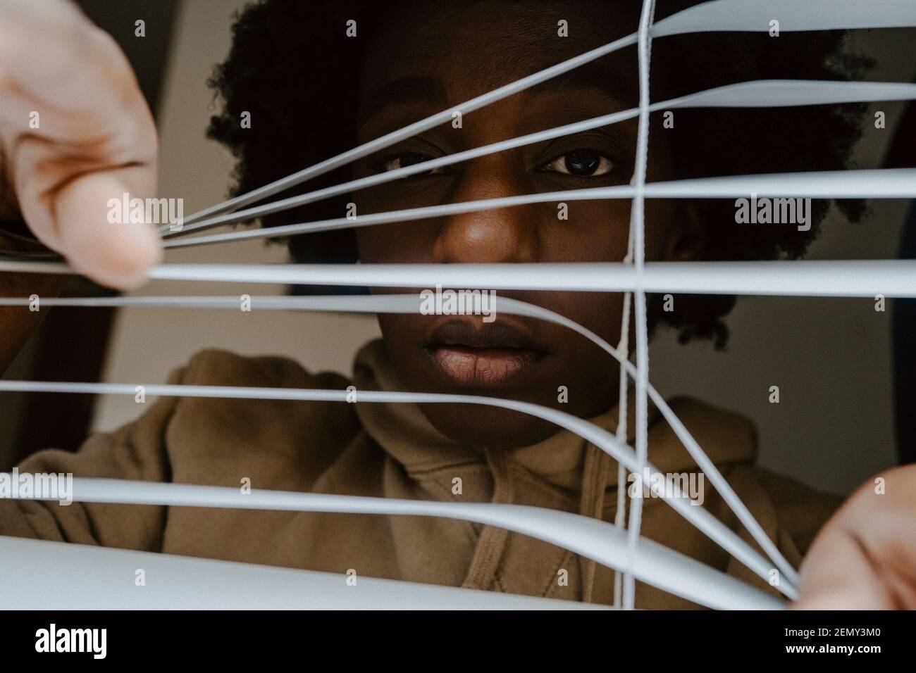 Portrait of woman looking through window blinds at home Stock Photo