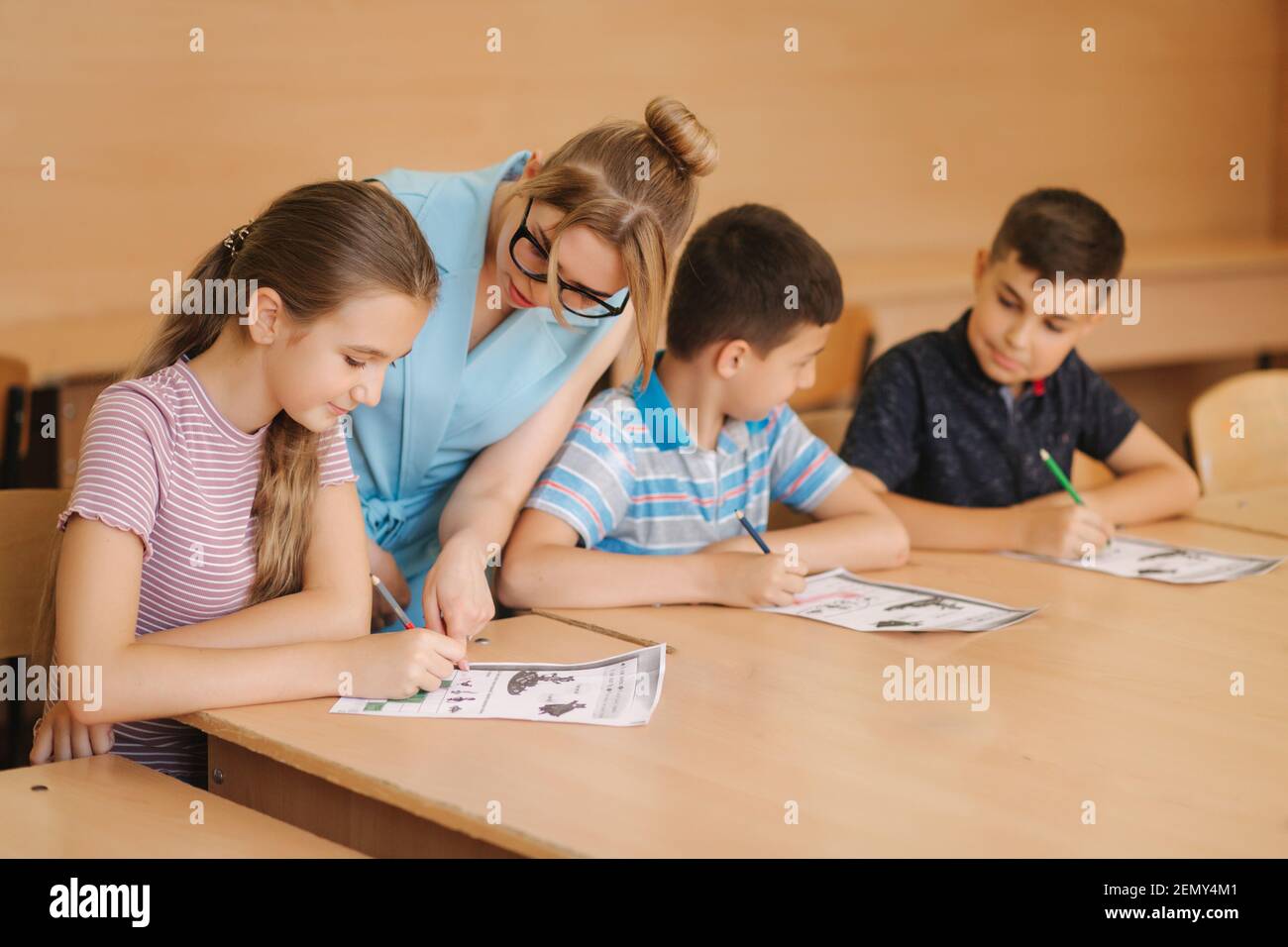 Teacher helping school kids writing test in classroom. education