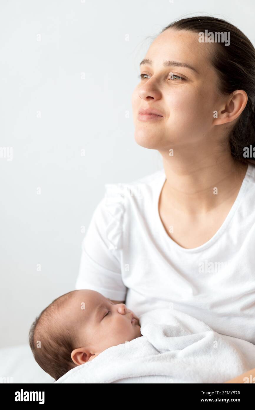close-up portrait of mom with newborn baby on white background copy space. Young cute caucasian woman black haired holding child in arms motherhood Stock Photo
