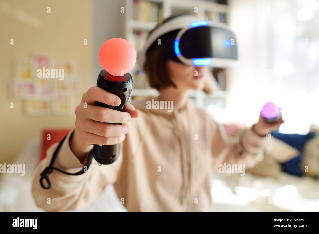 Pretty teenage girl wearing virtual reality headset at home. Cute teen using VR glasses to play a game. Child in virtual augmented reality helmet. Fut Stock Photo