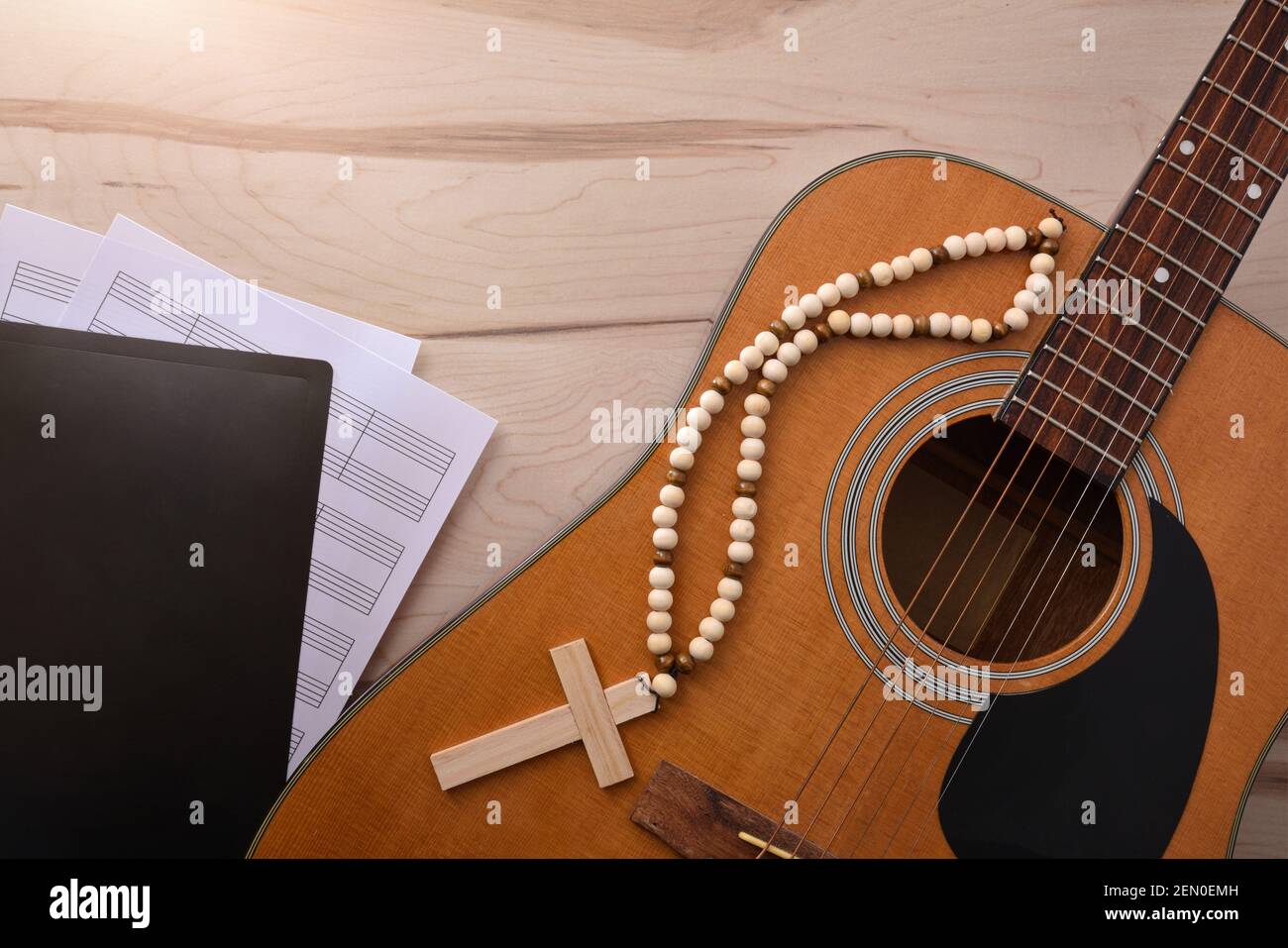 Acoustic guitar with wooden cross and songbook with religious scores on wooden table close up. Top view. Horizontal composition. Stock Photo
