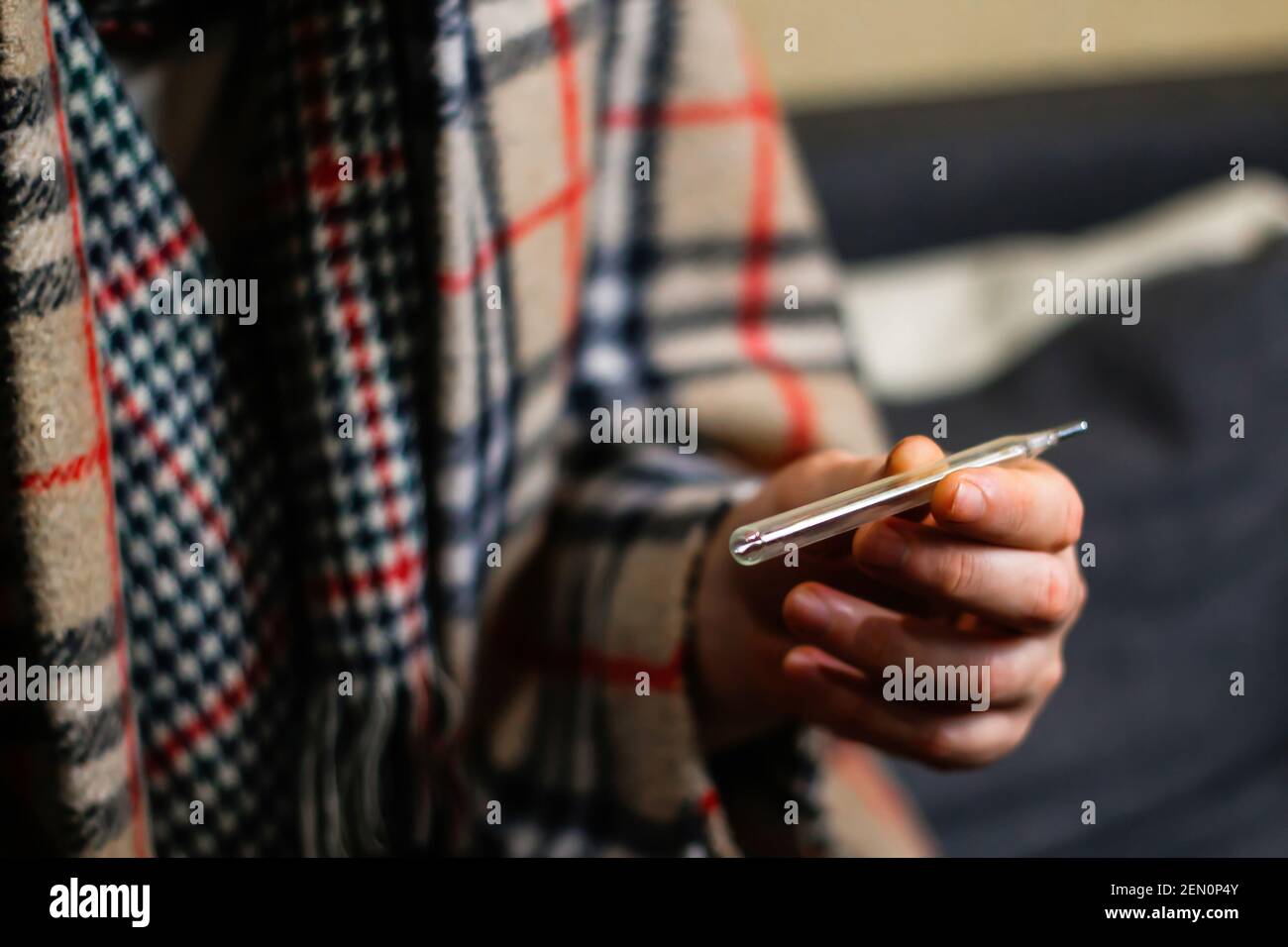 VV, Ukraine - 21.11.2020: defocus Guy measures the temperature. Faceless picture of sick man cold at home in warm checkered plaid, man's hand holding Stock Photo