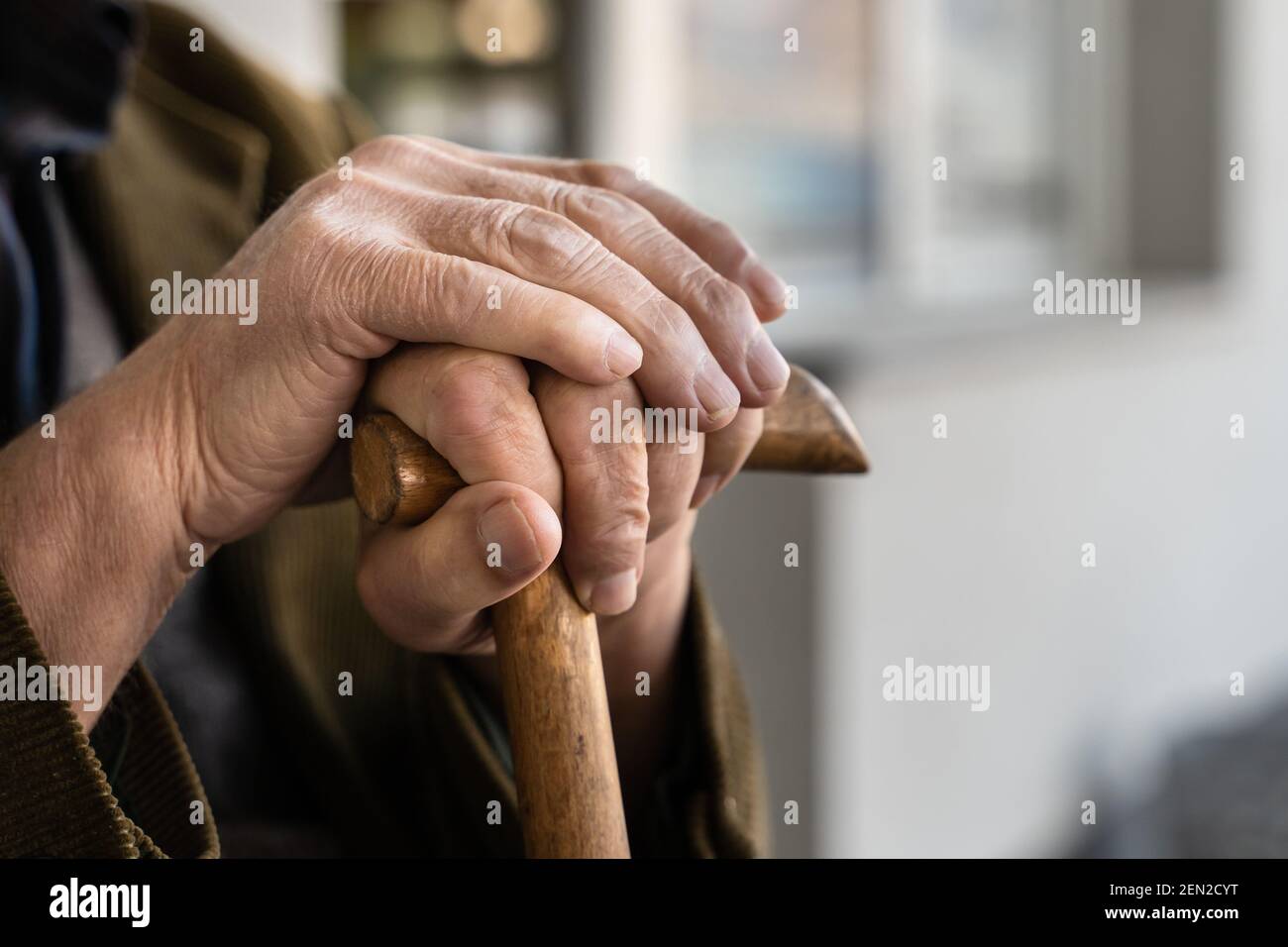 Close up on hands of unknown old caucasian man pensioner senior holding cane walking stick while sitting and waiting - real people old age senility co Stock Photo