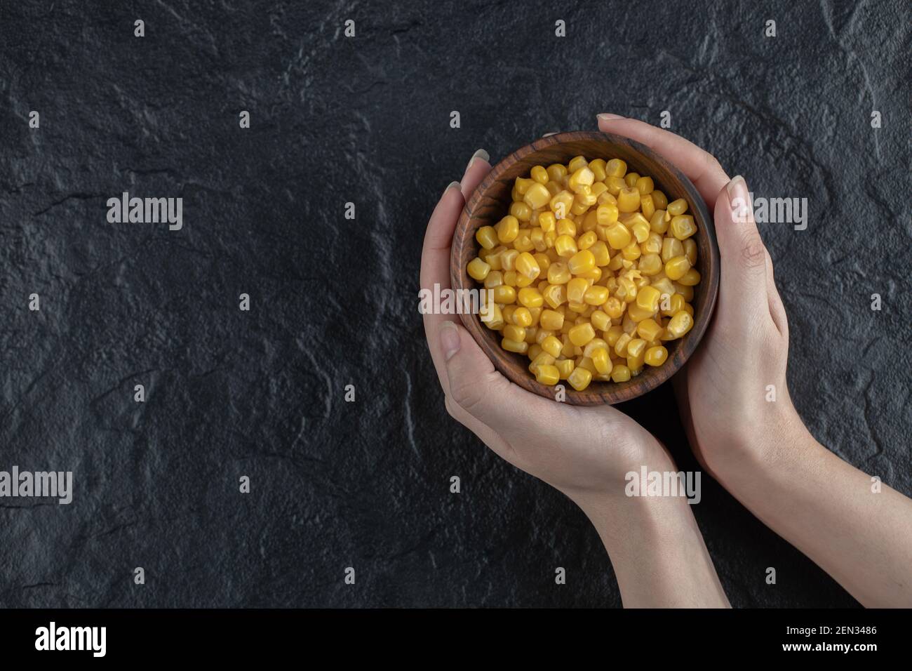 Female holding Canned sweet corn in bowl over black background Stock Photo