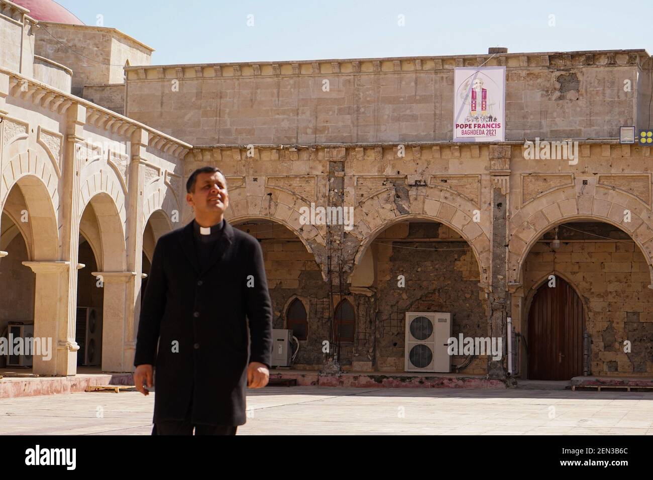 Qaraqosh, Iraq. 25 Feb 2021: Father Ammar Yako, the head of the church, walks past a poster of Pope Francis days before his historic visit to Iraq. Credit: SOPA Images Limited/Alamy Live News Stock Photo