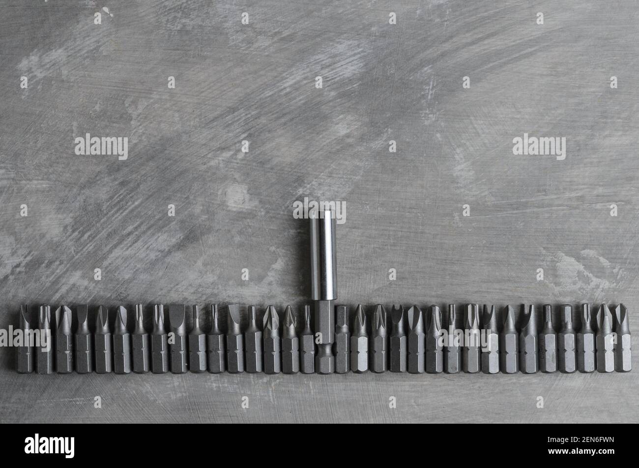 Screwdriver bits for various slots laid out in a row on a gray concrete surface. Stock Photo