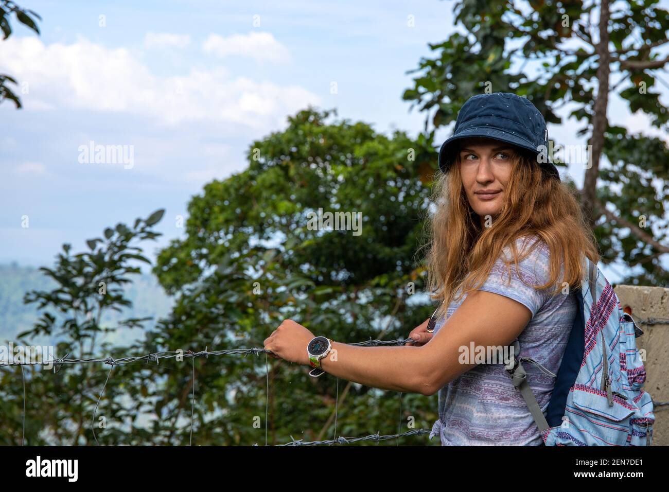 Young woman tourist in hat. Hiking in summer forest. Candid woman portrait in natural environment. Mountain viewpoint. Walking in green forest. Touris Stock Photo