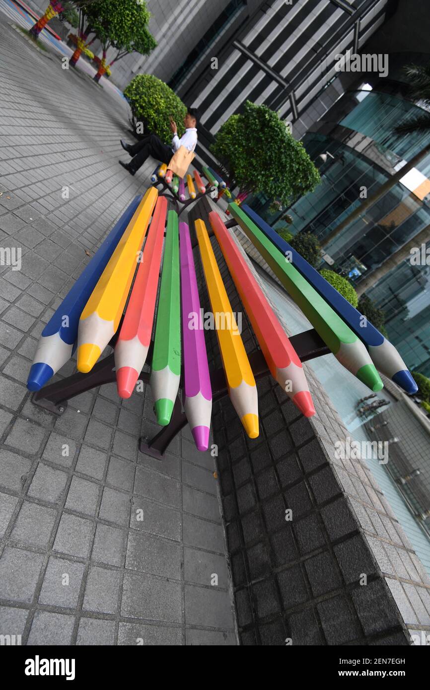A Chinese man sits on a colored pencil bench next to others at a square  amongst office buildings in Guangzhou city, south China's Guangdong  province, 23 June 2019. A square amongst a