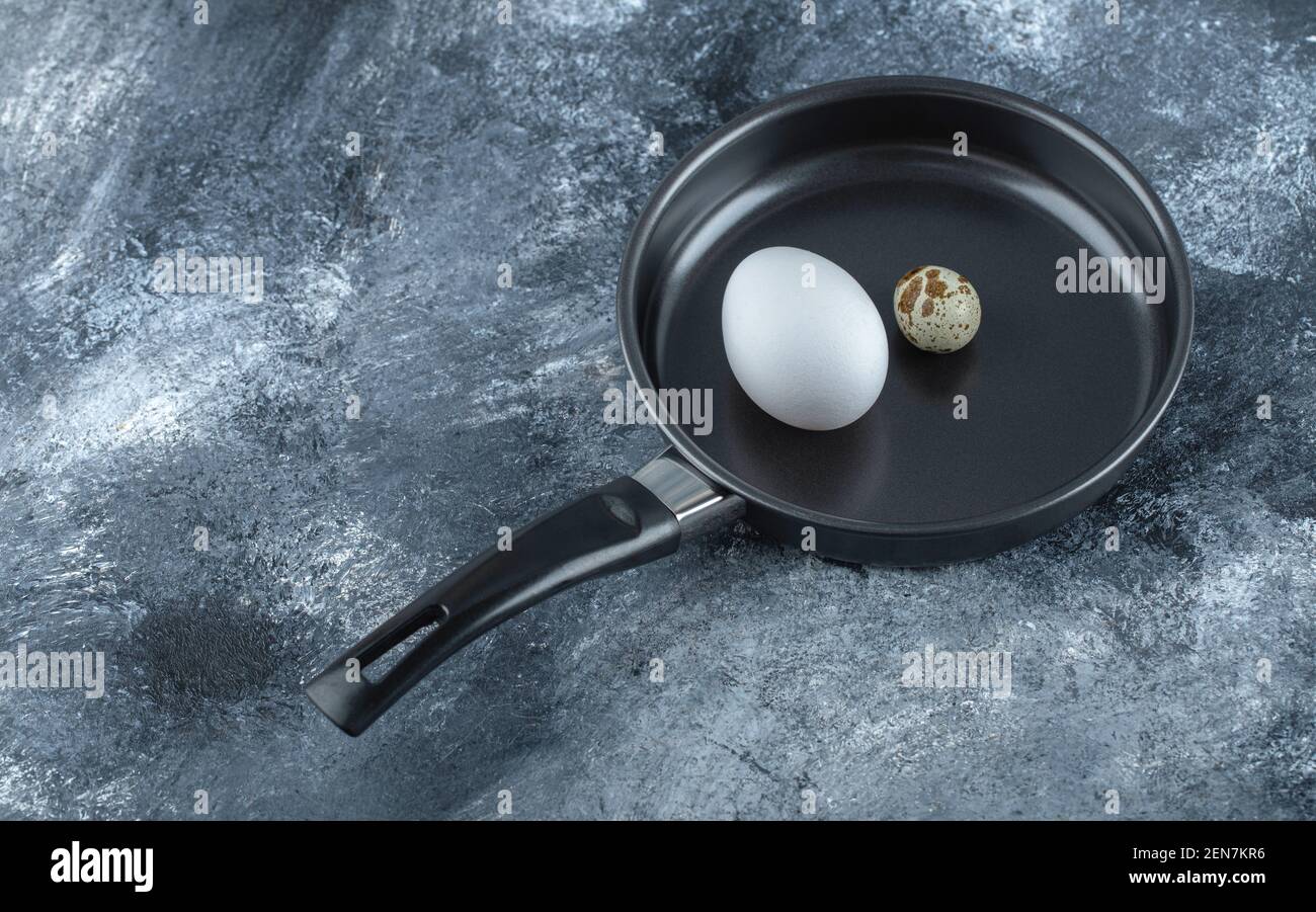 Fresh organic chicken and quail eggs in black frying pan Stock Photo
