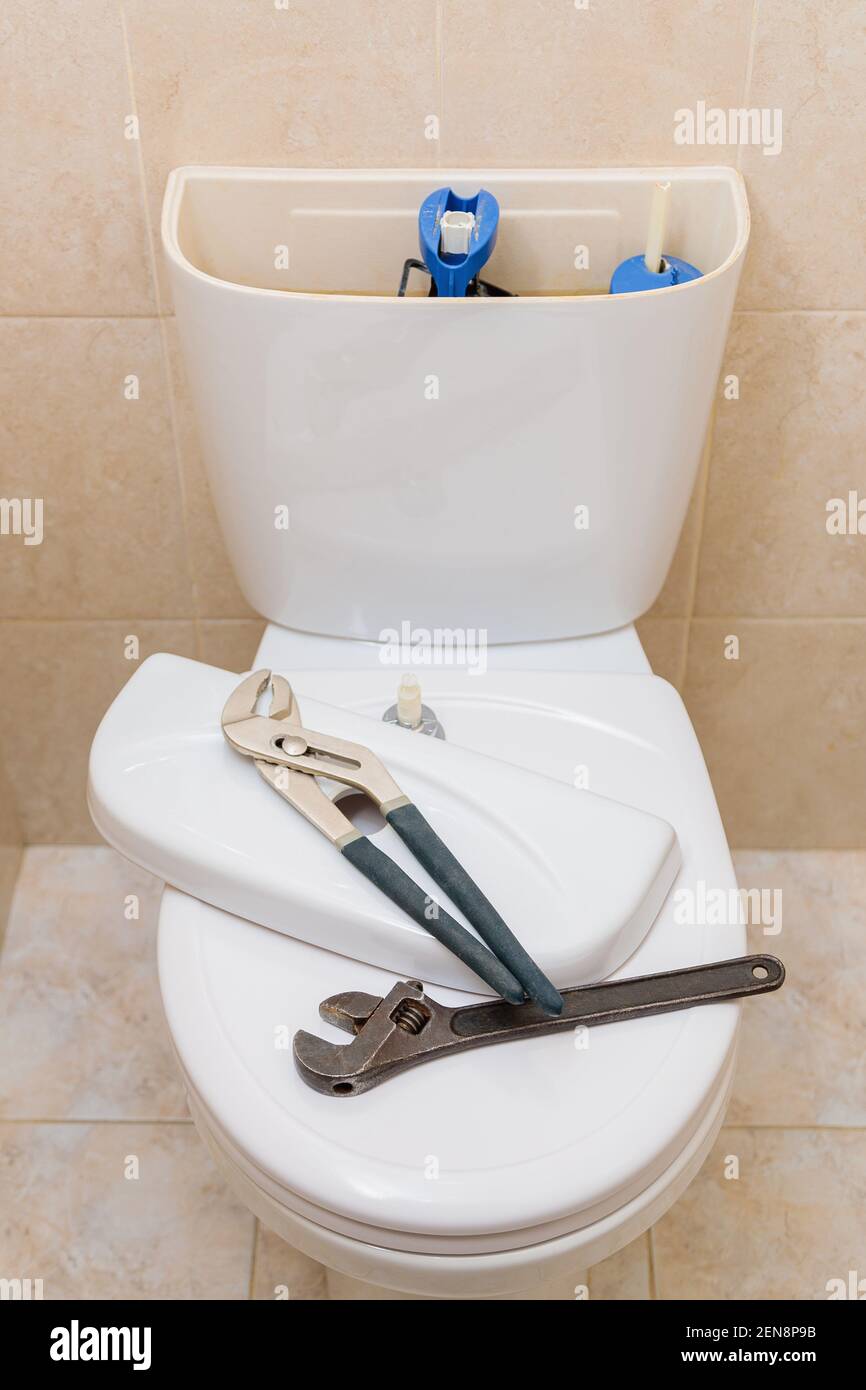 Plumbing tools in the toilet on a white toilet bowl. Drain tank cap removed Stock Photo