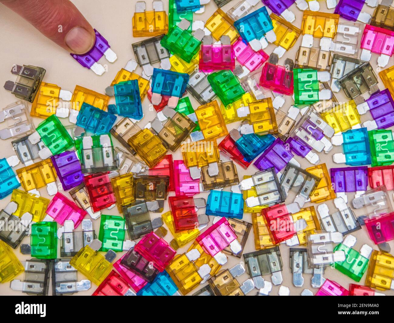 Closeup pov shot of a finger selecting a blade fuse of the required amp rating, from the colourful variety spread out on a flat surface. Stock Photo