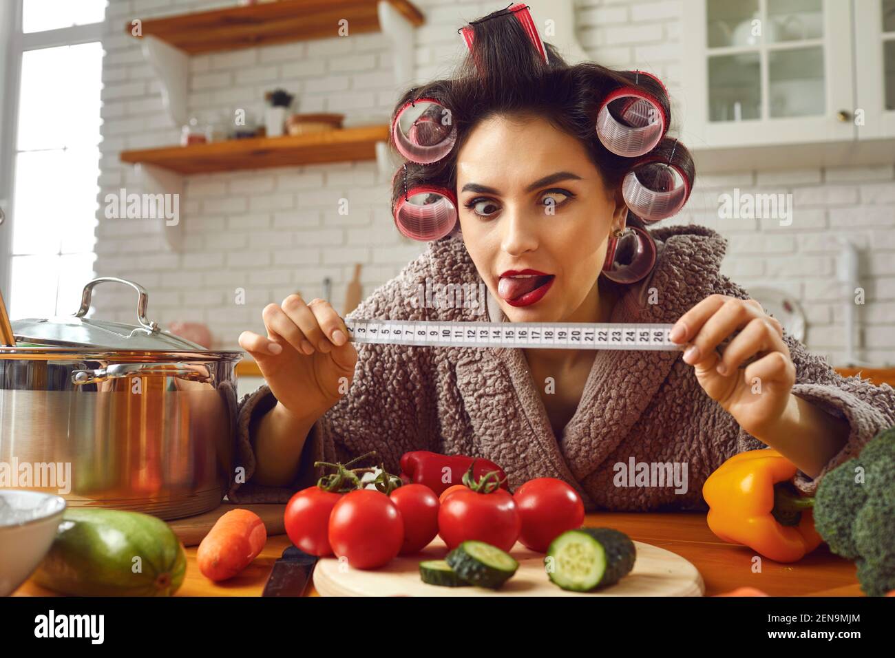 Funny crazy woman looking at tape measure while cooking healthy food in the kitchen Stock Photo