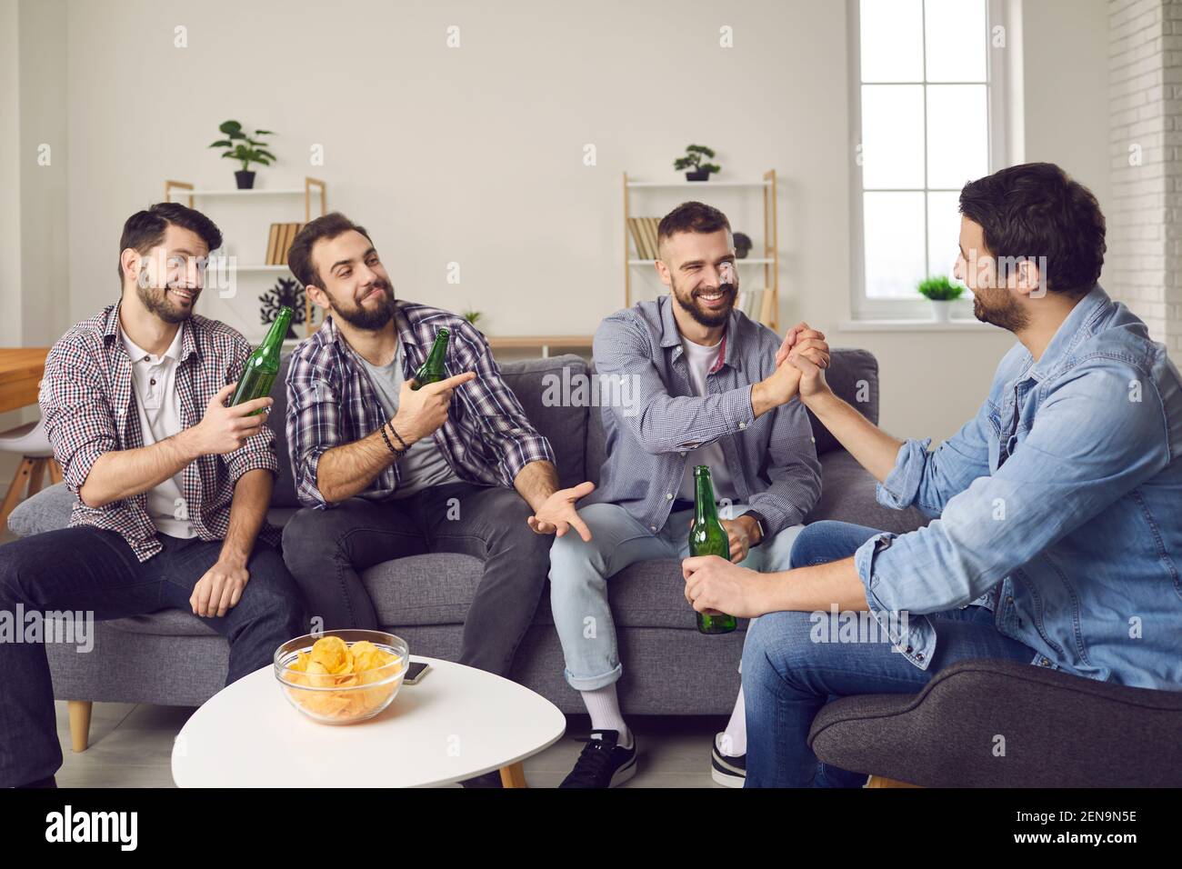 Group of friends sitting on couch, drinking beer and making fun bets with each other Stock Photo