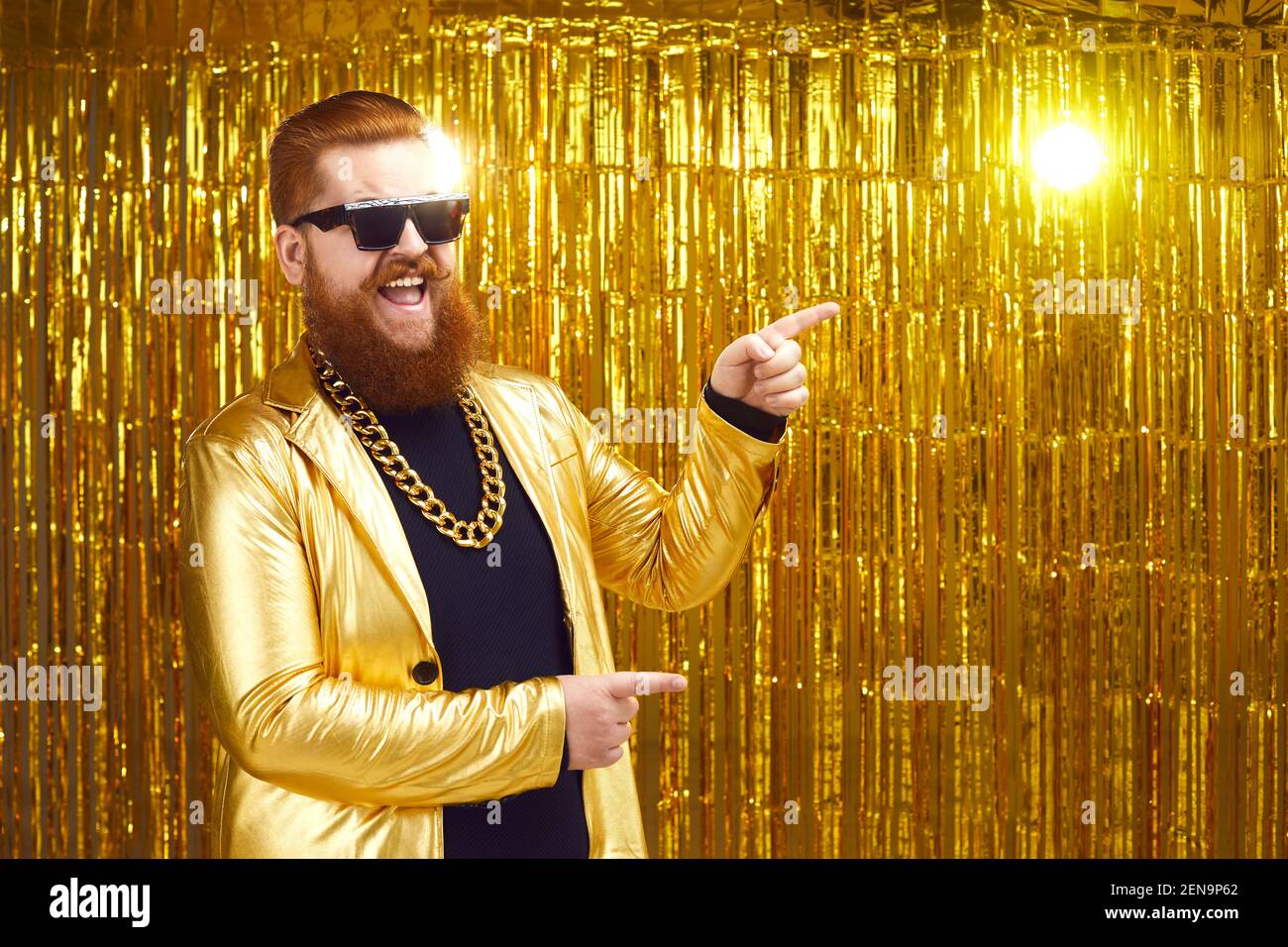 Happy man in extravagant party jacket and gold chain pointing to advertising copy space Stock Photo
