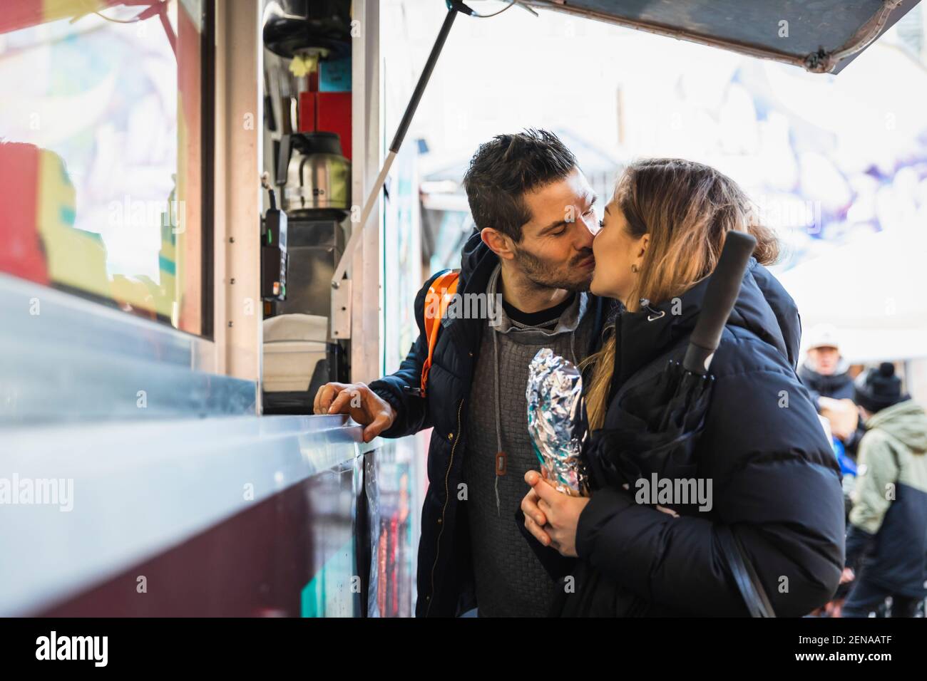 Heterosexual couple kissing while purchasing packaged order at sidewalk cafe Stock Photo