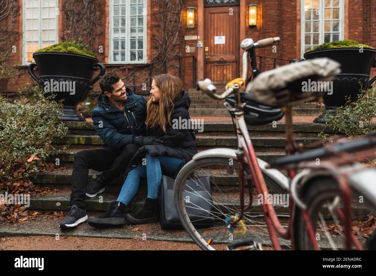 Smiling couple looking at each other while sitting on steps against house Stock Photo