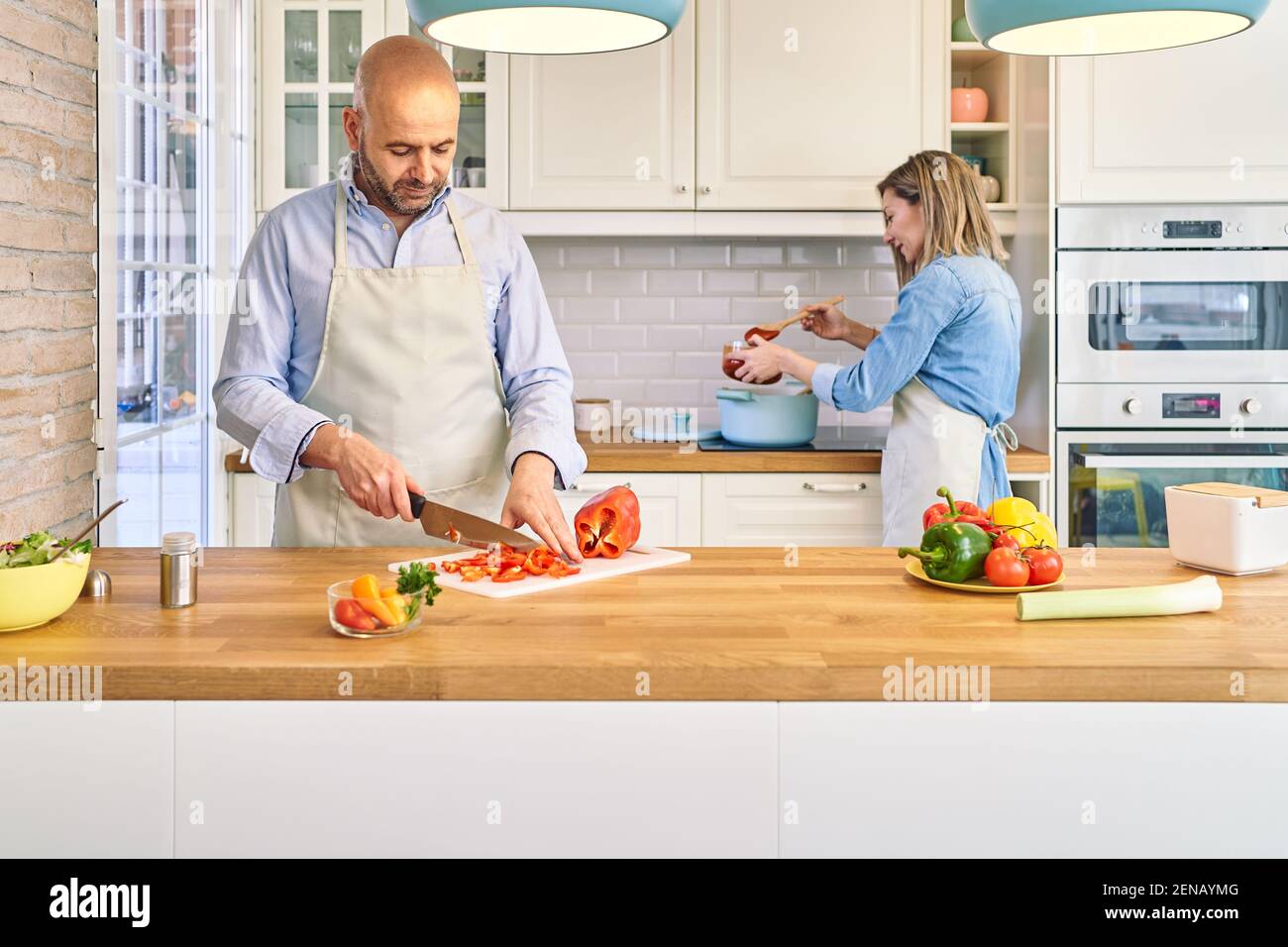 A happy young couple is enjoying and preparing a healthy meal. He cuts vegetables, she cooks spaghetti. . High quality photo Stock Photo
