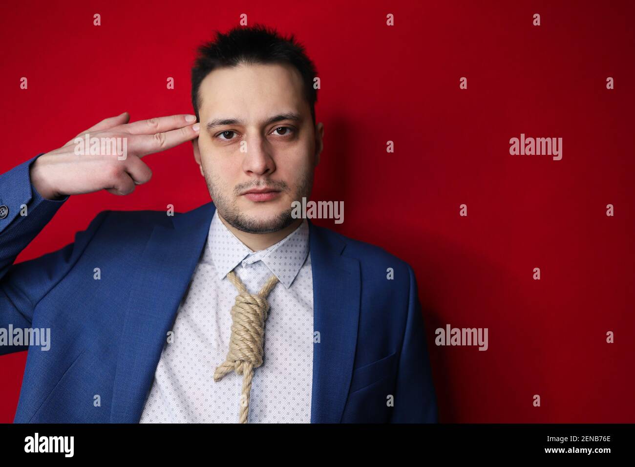 Concept image of business in trouble. Man in suit with Lynch loop instead of tie over neck. suicidal symbol of finger shot to head. Stock Photo