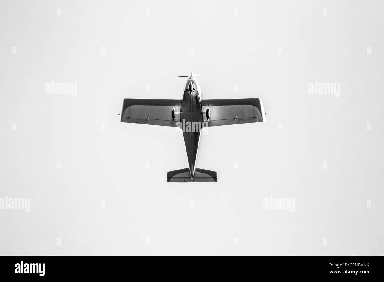 A black and white portrait of a small leisure airplane. You can see the bottom of the aircraft which is flying by with a blue sky. Stock Photo
