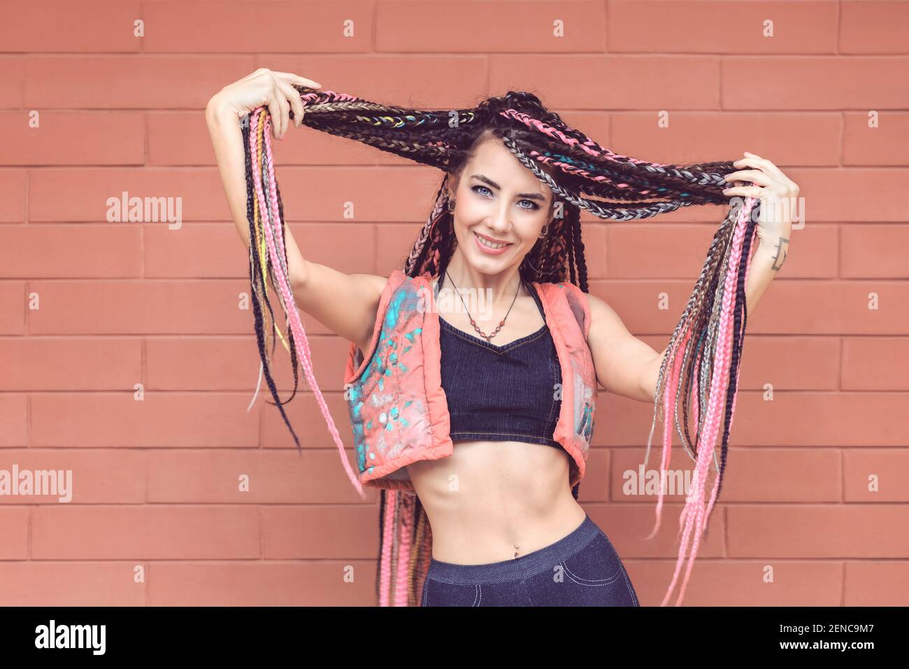 Modern teenage girl with colorful dreadlocks on wall background Stock Photo