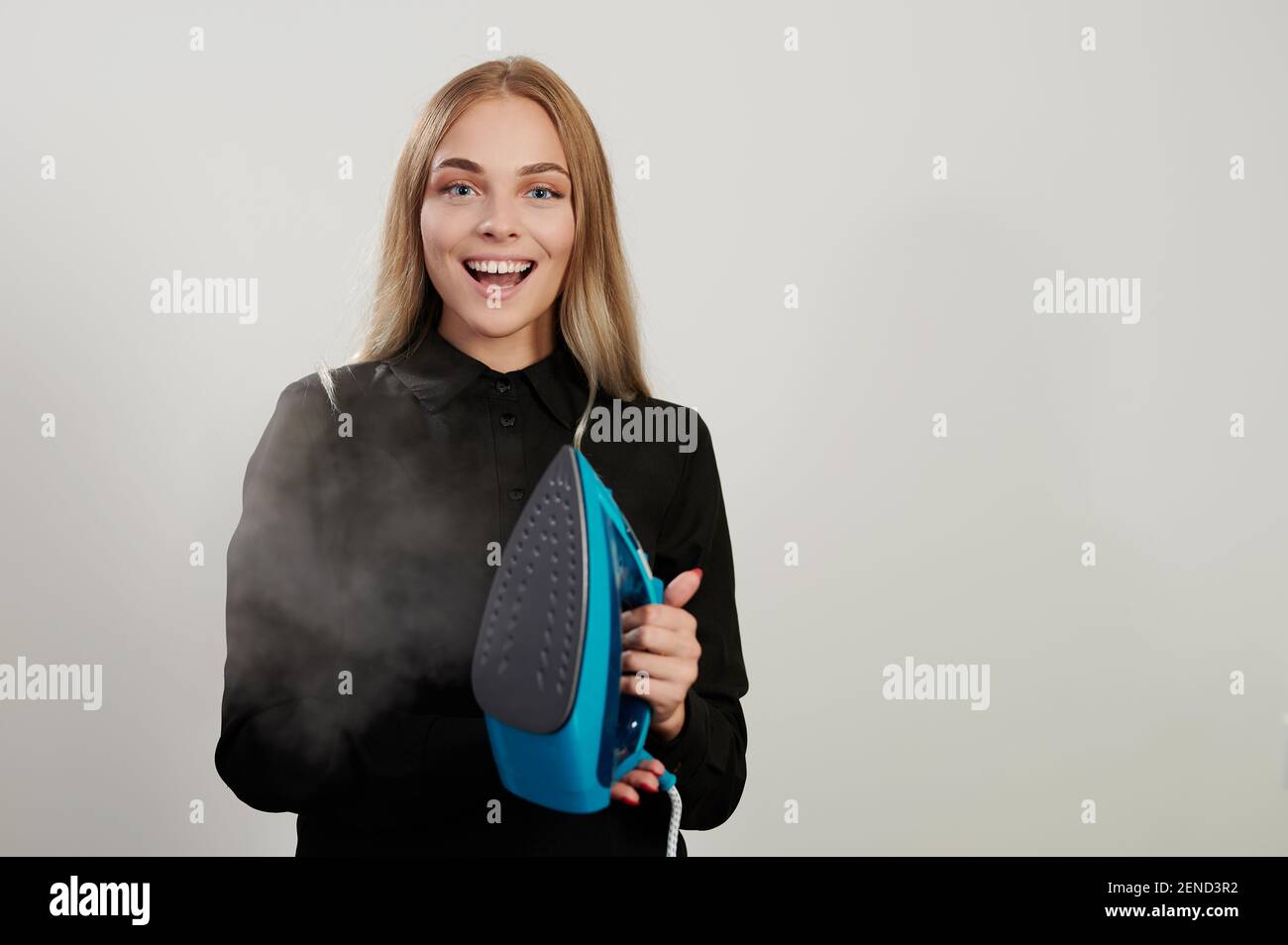 Pretty smiling girl with iron and steam isolated on white studio background Stock Photo