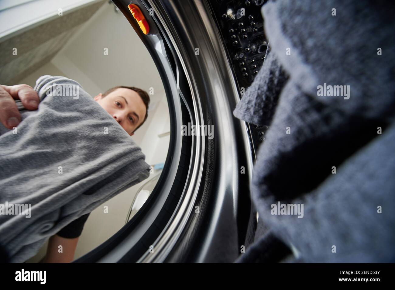 Man loading dirty cloth to washing machine view from inside Stock Photo