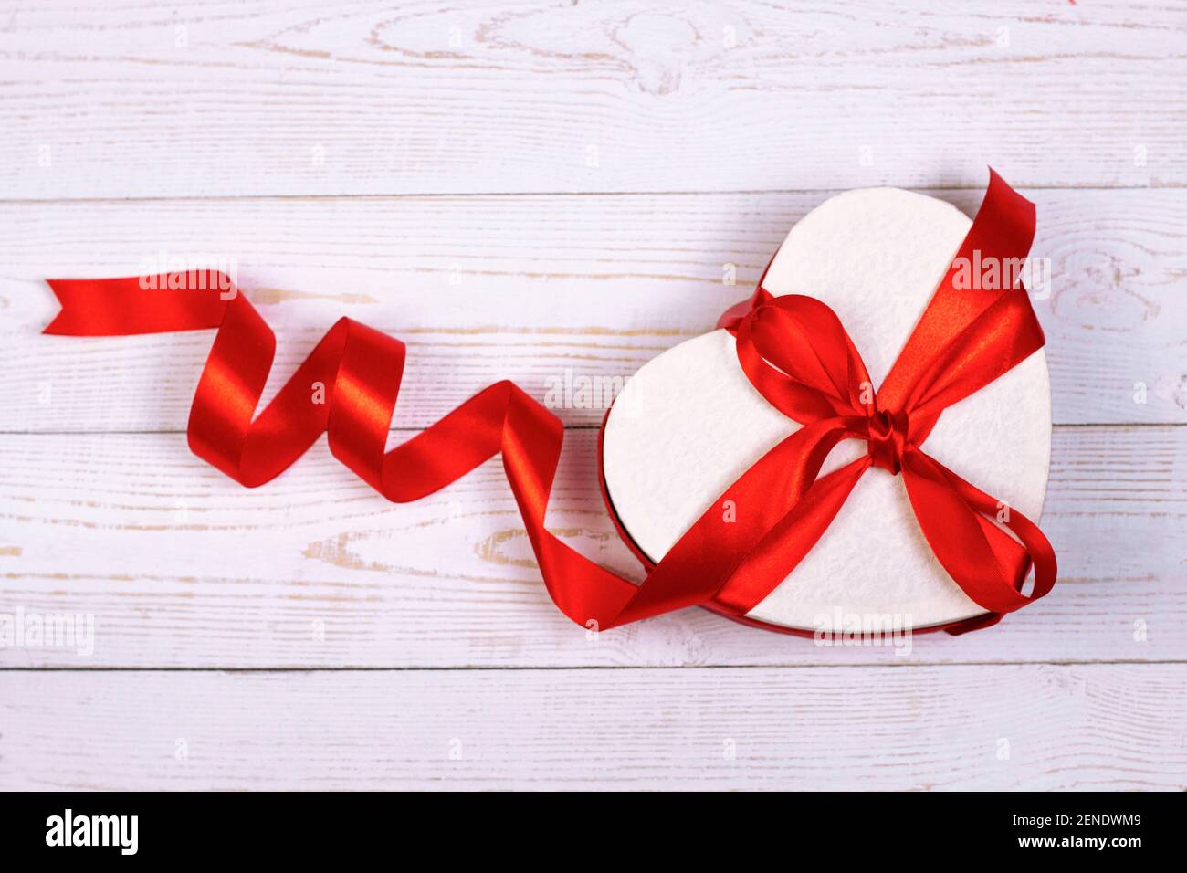 Heart shaped gift box with red ribbon on white wooden background ...