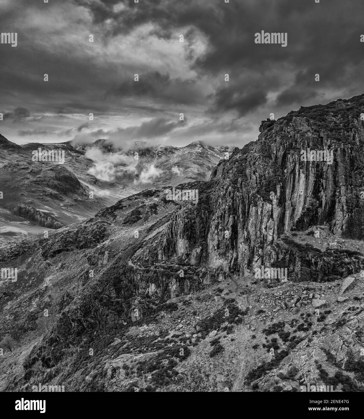 Epic flying drone  black and white landscape image of Langdale pikes and valley in Winter with low level clouds and mist swirling around Stock Photo
