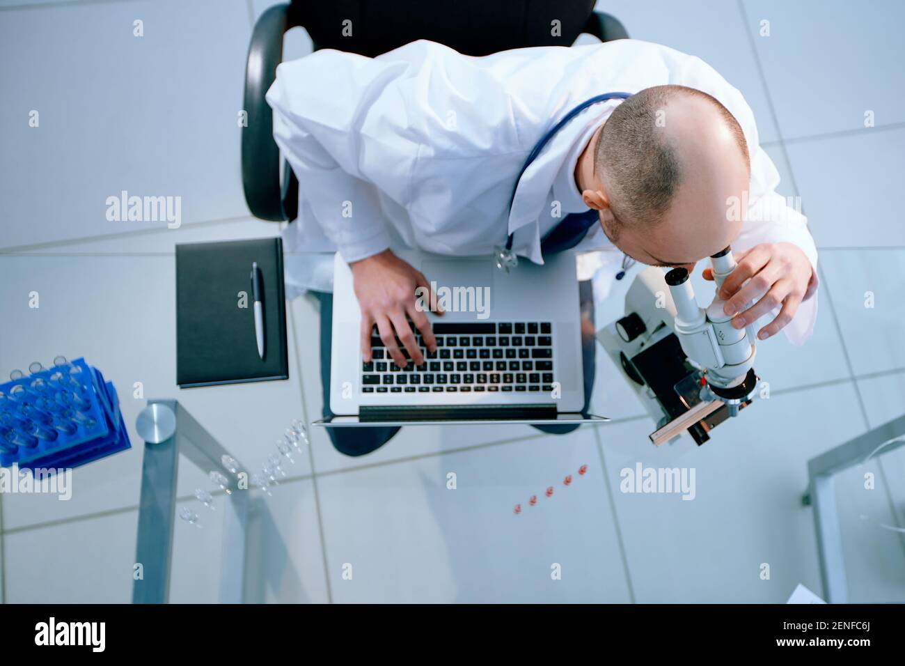 scientist looking through a microscope and using a laptop during his research. Stock Photo