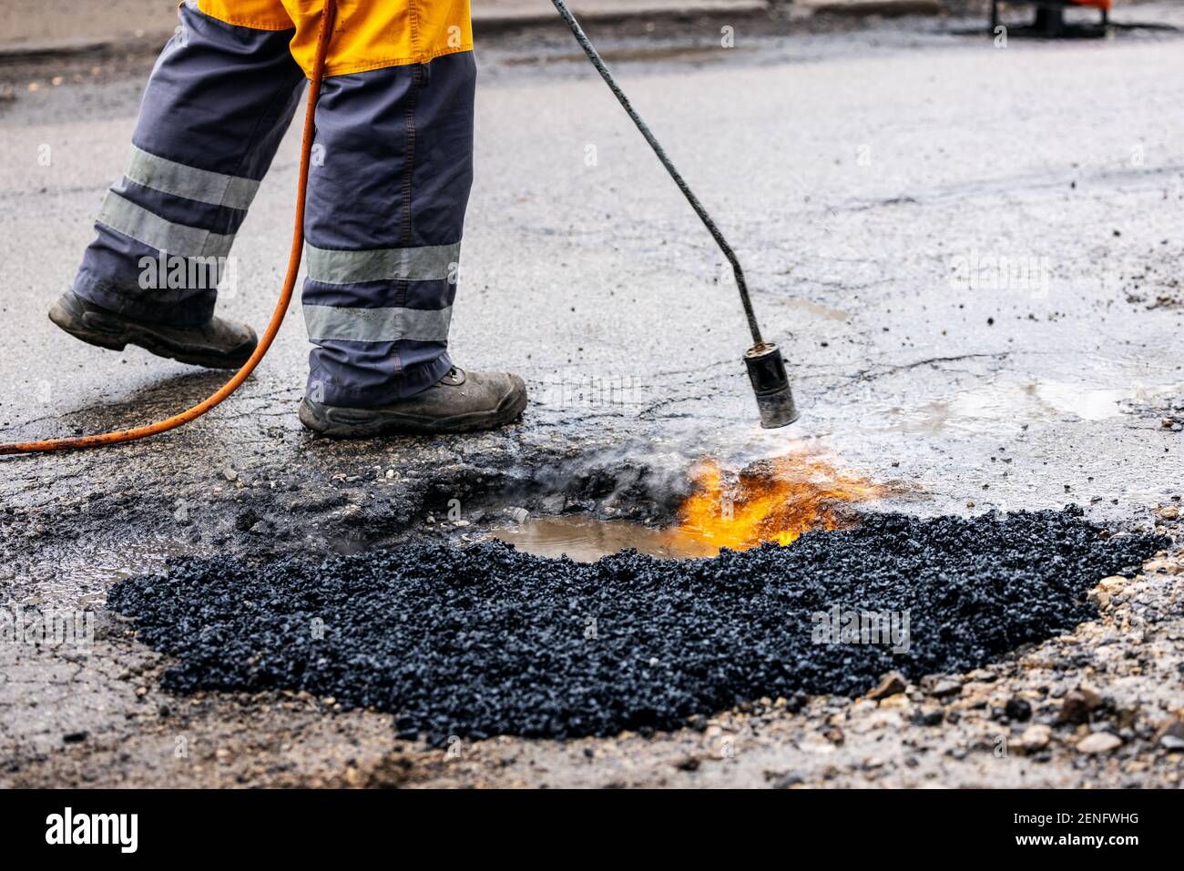 worker repairing pothole with bitumen asphalt on the road Stock Photo