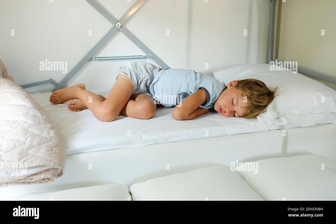 Child in pajamas sleeping in his bed without blankets, illuminated