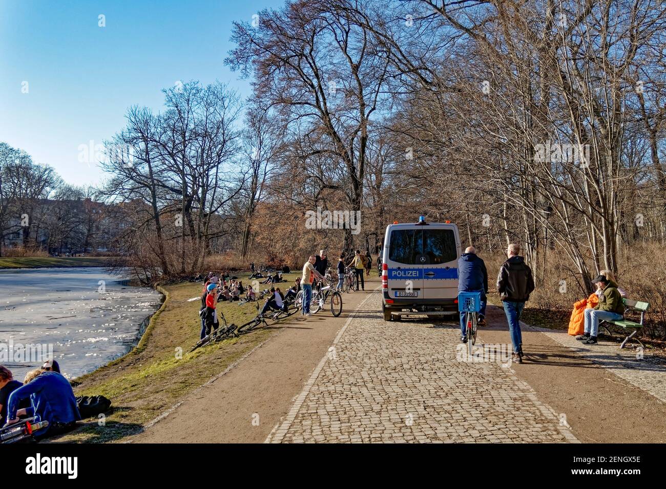 Vorfruehling in Berlin Mitte Februar 2021 , Treptower Park, Junge Leute geniessen das milde Fruehlingswetter am Karpfenteich. Polizei kontrolliert die Stock Photo