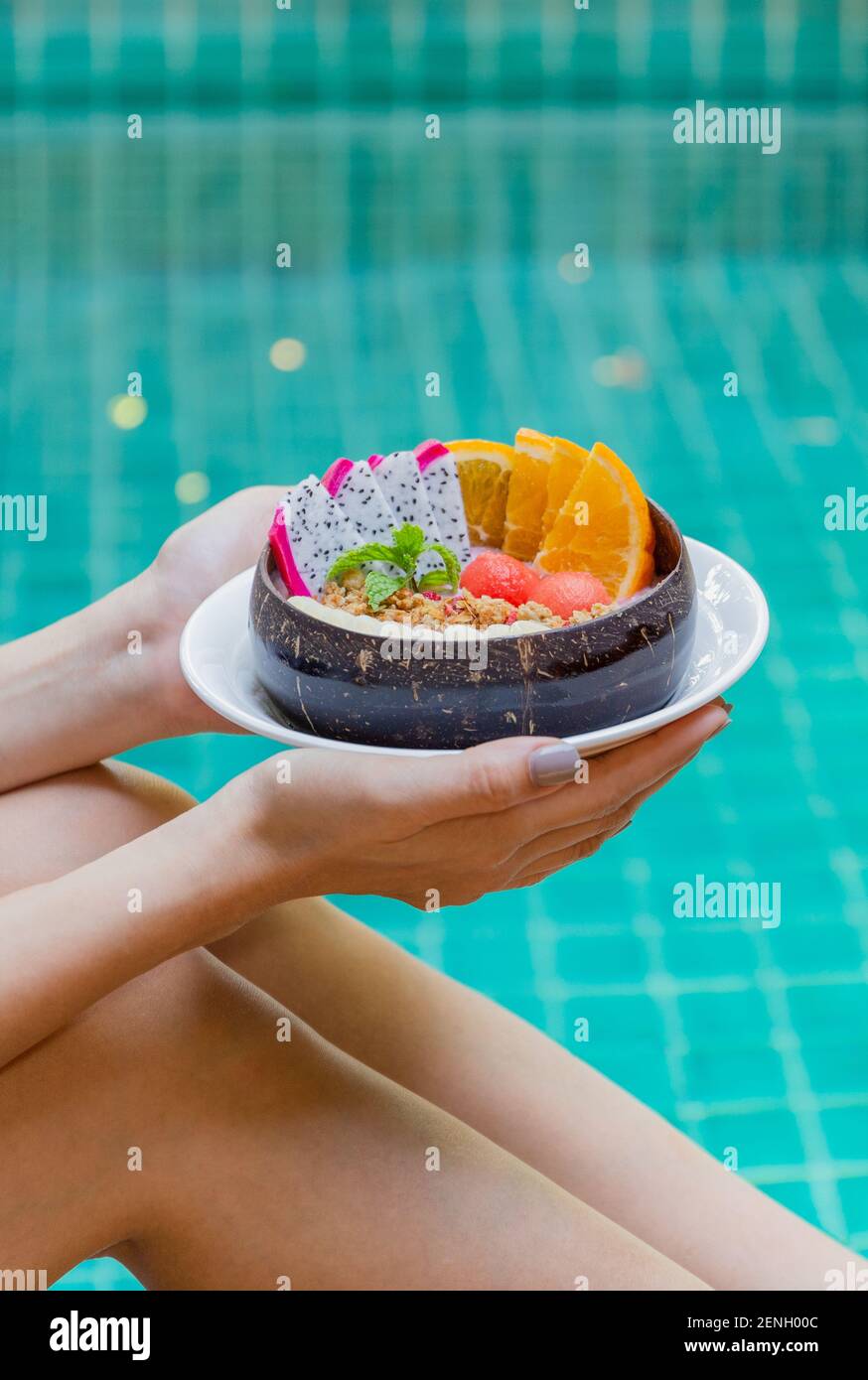 Woman holding smoothie bowl and fruits by swimming pool. Stock Photo