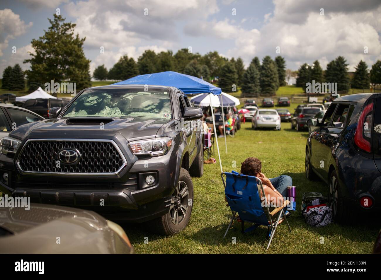 A Woodstock attendee tailgates near a large truck in the parking lot at